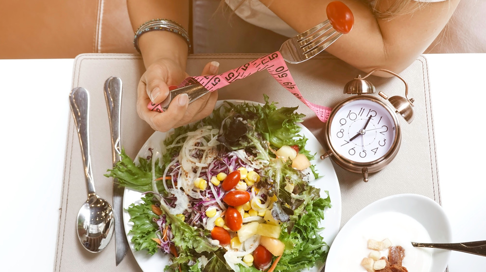 woman eating salad near clock, tape measure