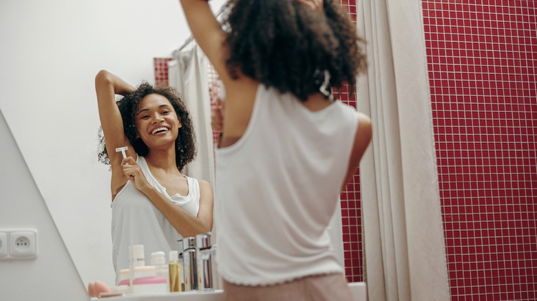 Woman shaving armpits with razor in mirror