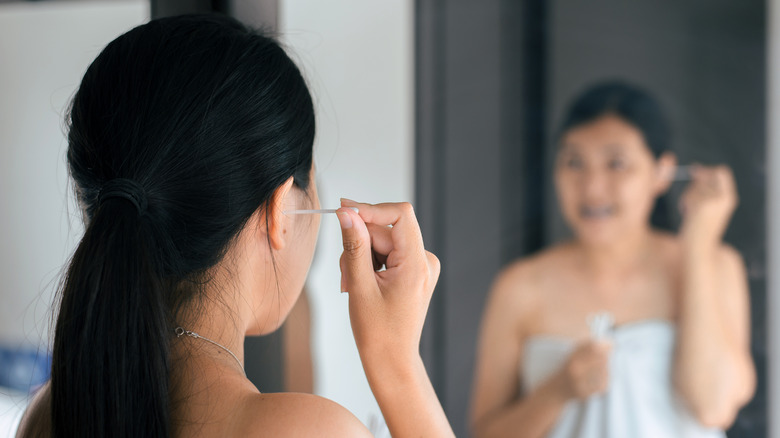 Young woman using cotton swab in ear