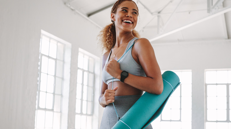 woman smiling carrying yoga mat