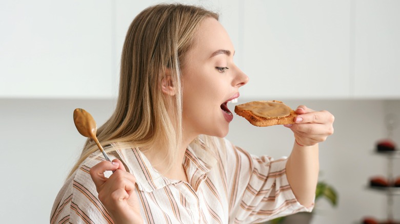 A woman eating a slice of bread with peanut butter