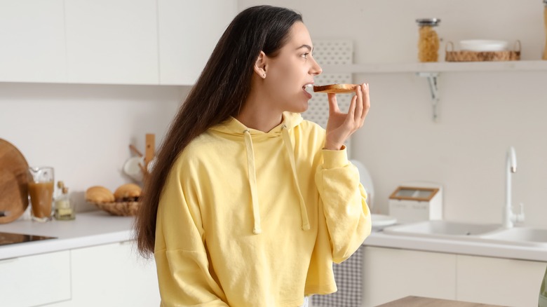 A woman eating a slice of toast with peanut butter