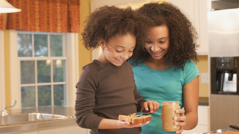 A young girl spreading peanut butter on bread