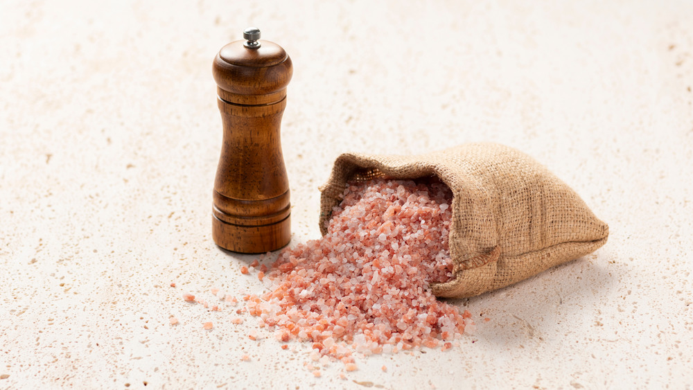 pink sea salt overflowing from burlap bag next to grinder