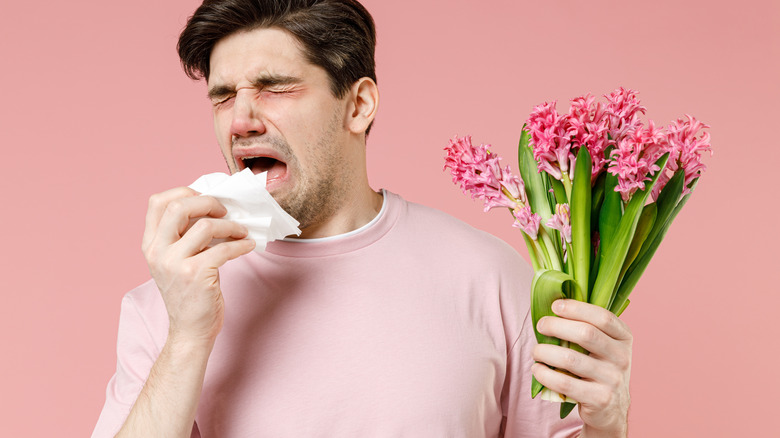 Man holding flowers and sneezing