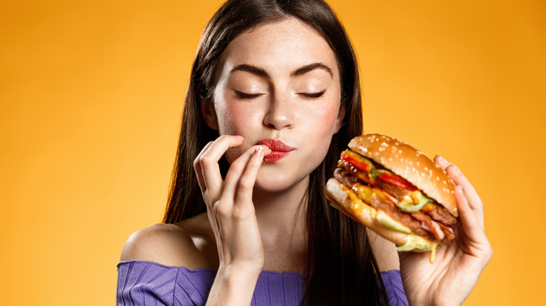 Woman eating cheeseburger with yellow background