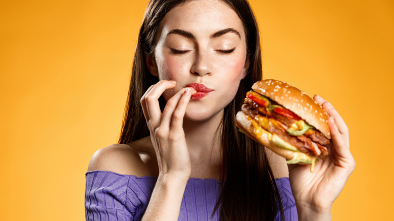 Woman enjoying cheeseburger with yellow background