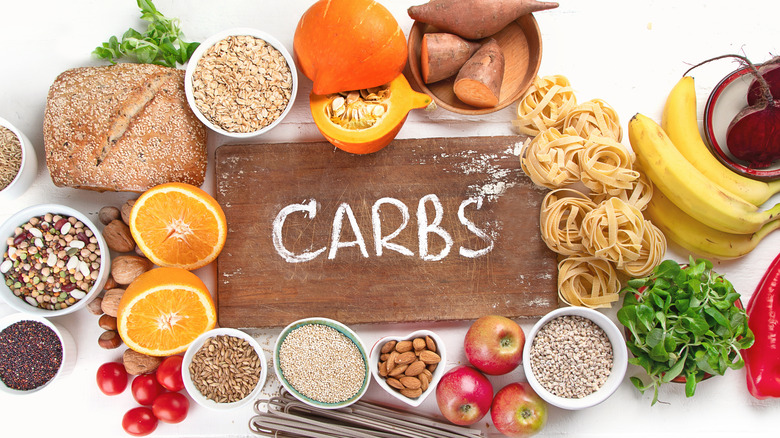 the word 'carbs' written on board surrounded by fruits, vegetables, whole grains