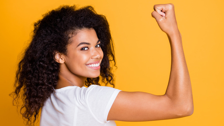 Woman flexes biceps with yellow background