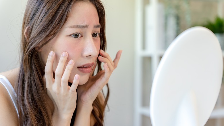 Woman looking into a hand mirror with a worried expression