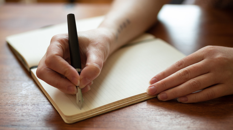 Hands writing in a journal that sits on a table