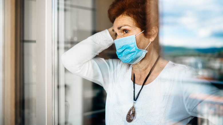 Older woman wearing a mask and looking out a window