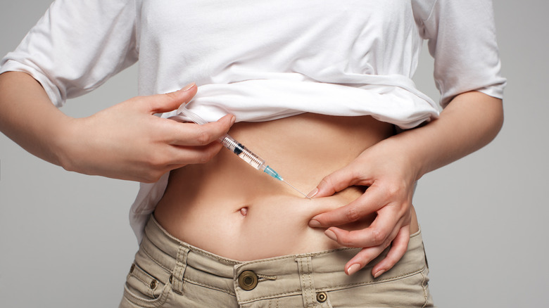 Woman with her shirt rolled up giving herself an injection in the belly
