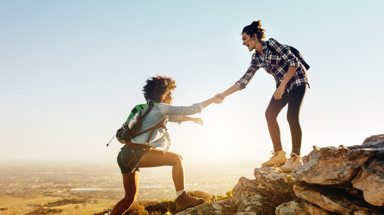 woman helping her friend climb a mountain