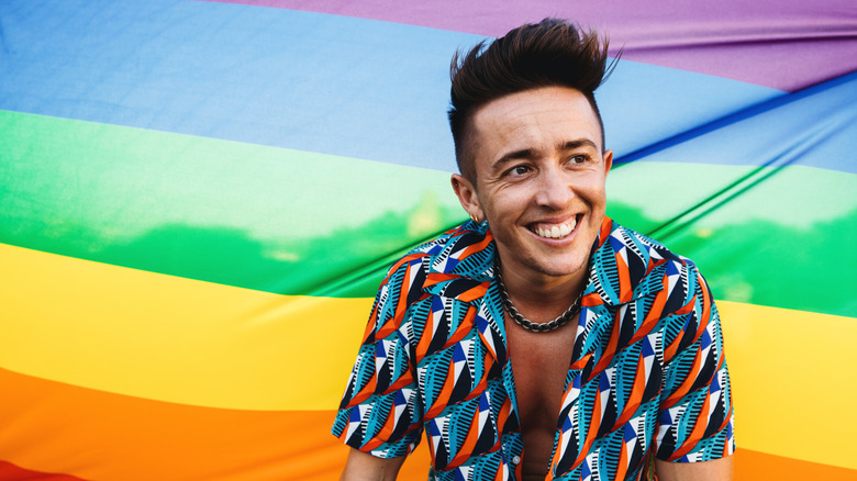 Trans man standing in front of a rainbow flag smiling