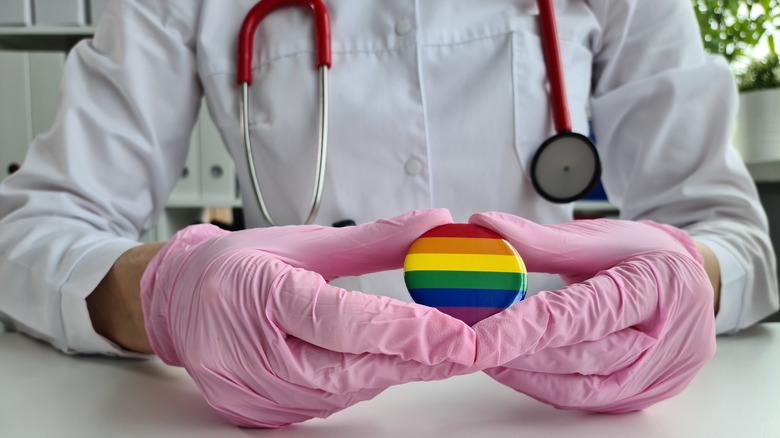 Doctor wearing pink gloves holding a rainbow pin, LGBTQ+ healthcare