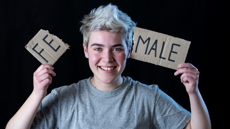 Young trans man holding a broken sign that used to say "female," now says "male"