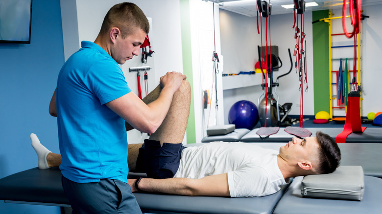 male physical therapist helping young man exercise knee