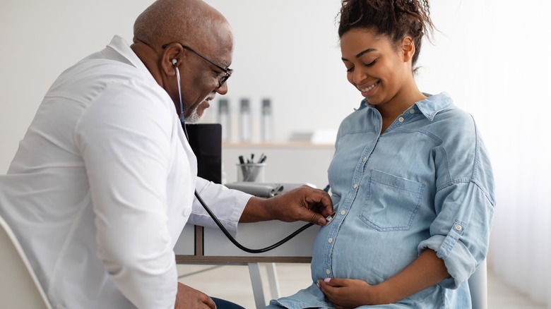 doctor placing stethoscope on pregnant woman's belly