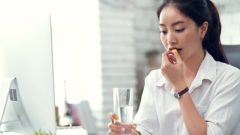 Woman holding a glass of water and taking a pill