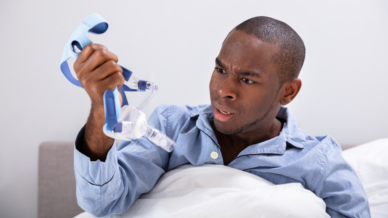 Man holding a CPAP mask and looking frustrated