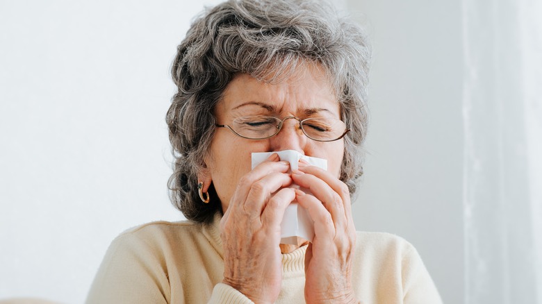 Older woman blowing nose and looking uncomfortable