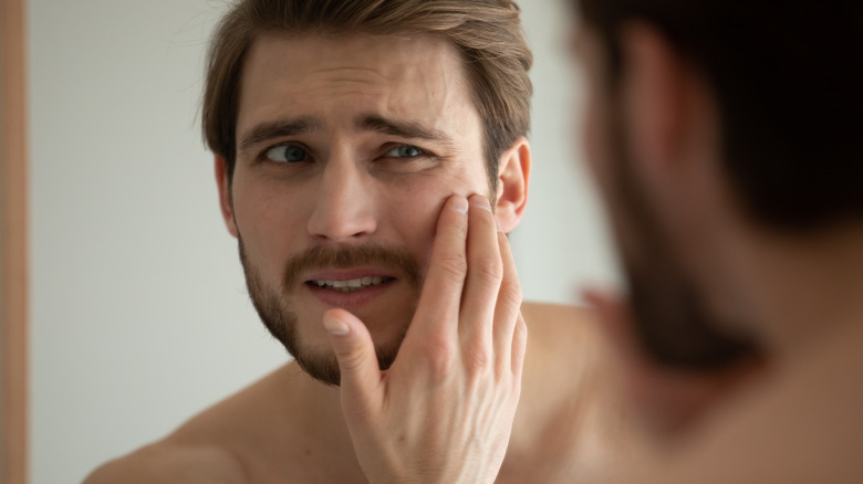 man looking at skin in the mirror