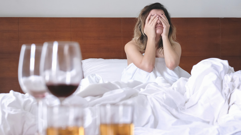 woman with hangover in bed with alcohol in room