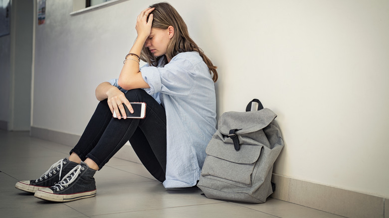 upset girl holding cell phone with backpack beside her