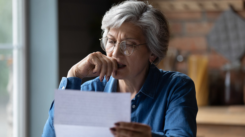 stressed older woman looking at bills in her kitchen