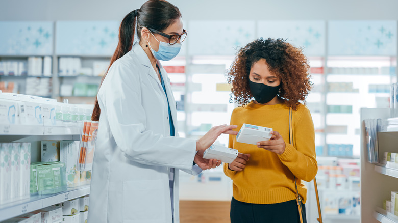 Pharmacist looking at drugs with customer