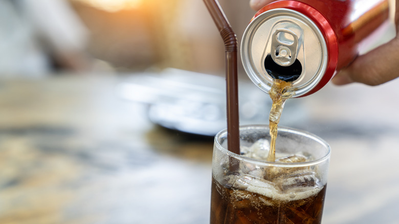 A can of Diet Coke pouring into a tall glass