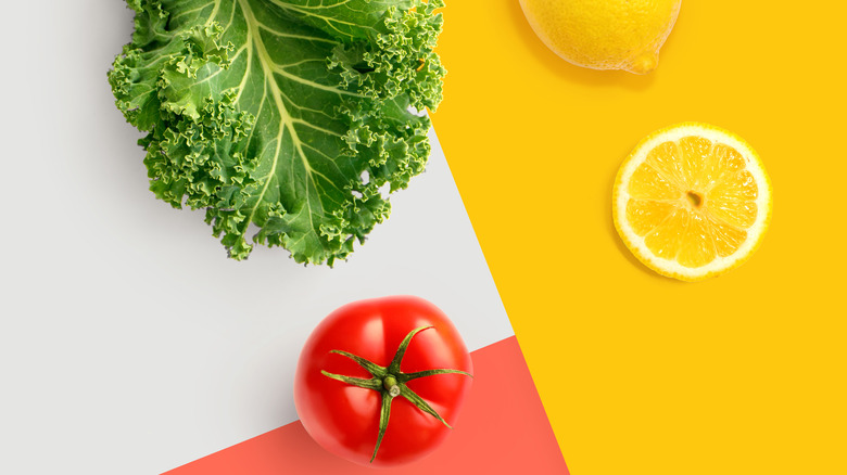 A leave of kale next to a slice of lemon, a whole lemon, and a tomato