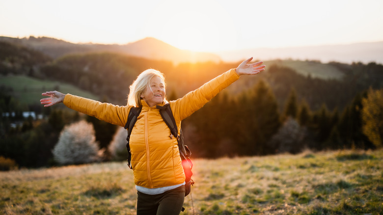 older woman walking outdoors with her arms outstretched and happy