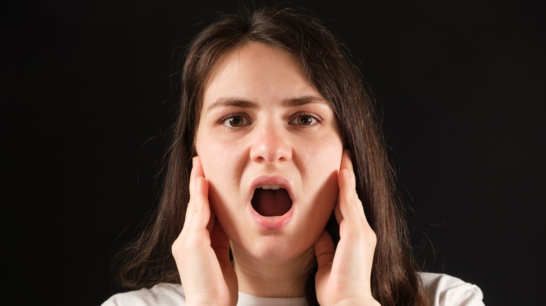 a woman holds her jaw with open mouth 