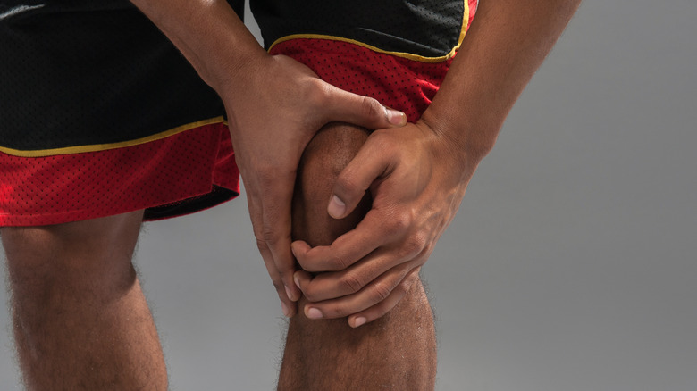 man holding knee in basketball shorts