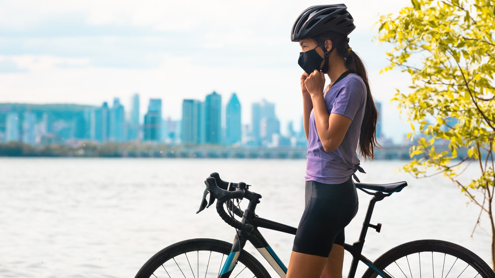 A woman fixes her face mask before cycling outdoors