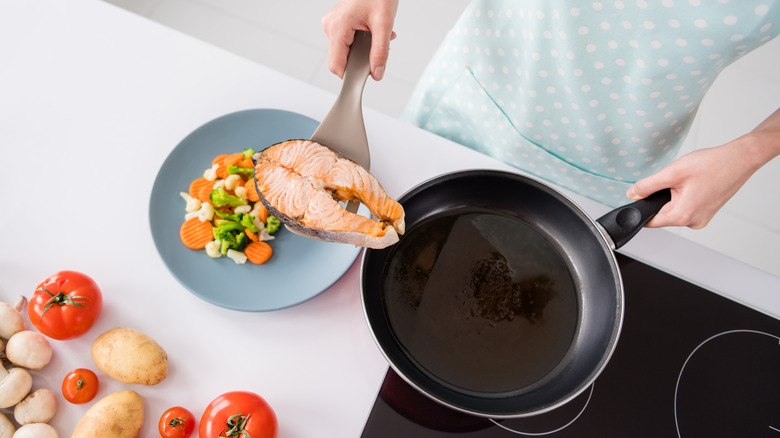 woman placing salmon on her plate of vegetables