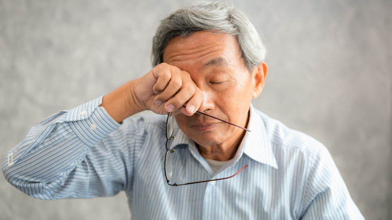 Asian man holding glasses rubbing eyes