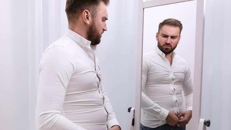 Man with excess belly fat looking in the mirror
