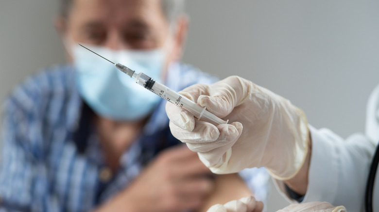 close-up of vaccine needle with senior man in background