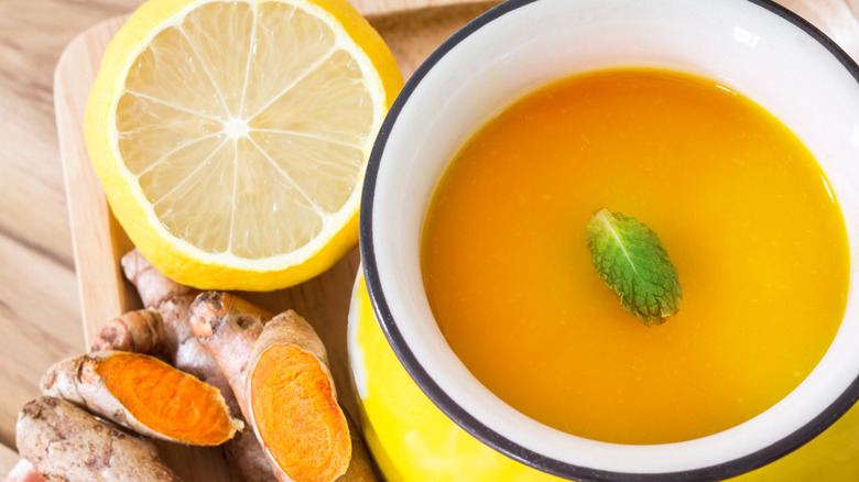 a yellow mug of golden milk beside a slice of lemon and ginger root