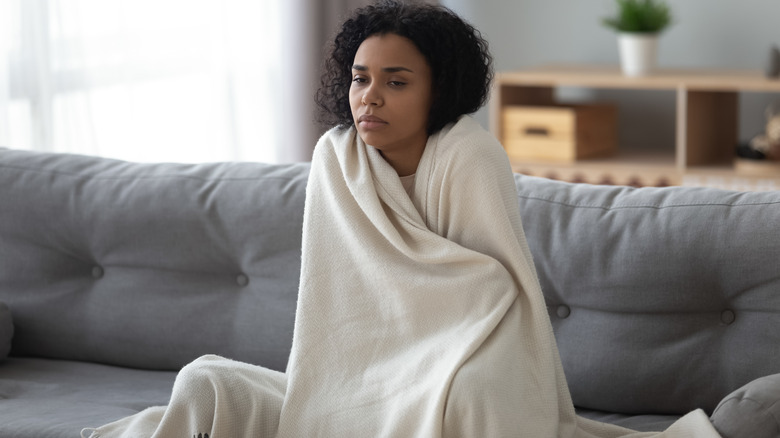 sick woman wrapped in blanket on couch