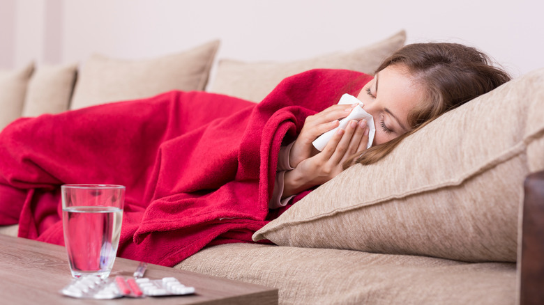 sick woman laying on couch with glass of water