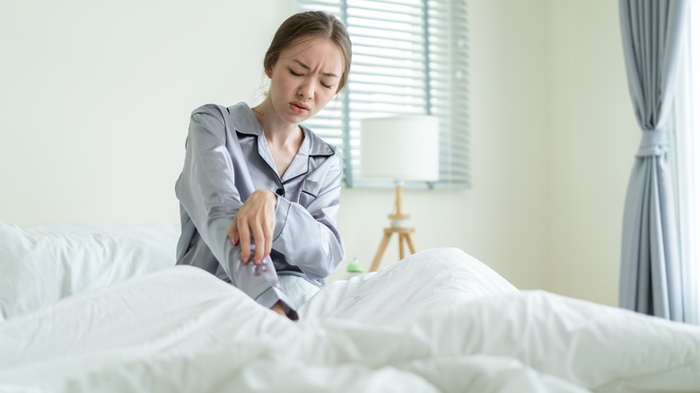 Woman sitting in bed scratching her arm