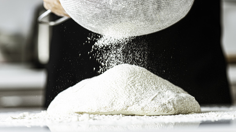 Baker sieving white flour to make bread