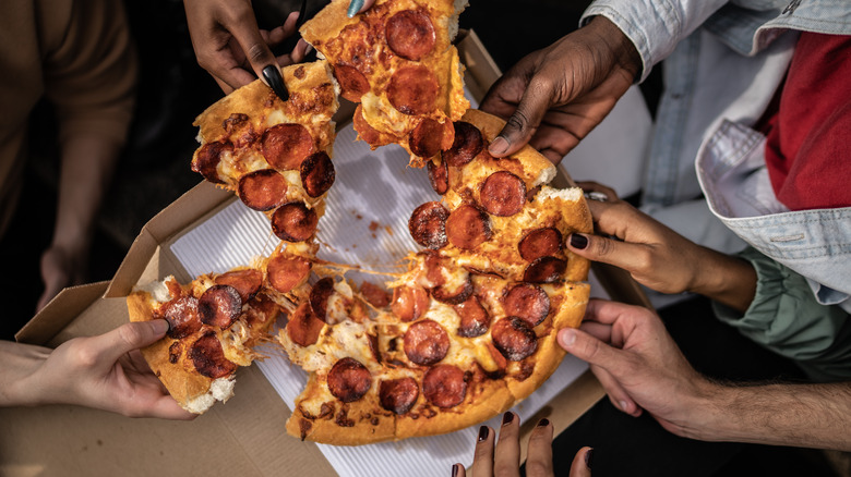 several hands pulling apart a pepperoni pizza