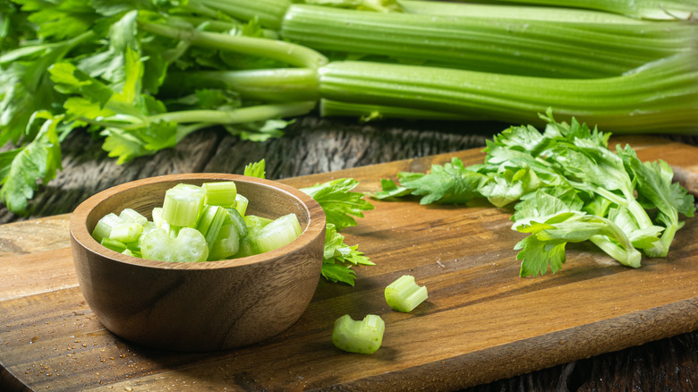 A wooden bowl filled with slices of celery and whole celery in the background