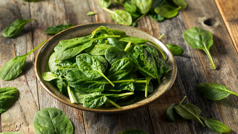 A bowl of spinach leaves on a wooden surface 