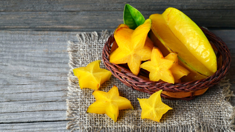 A basket with a whole star fruit and slices of star fruit next to it